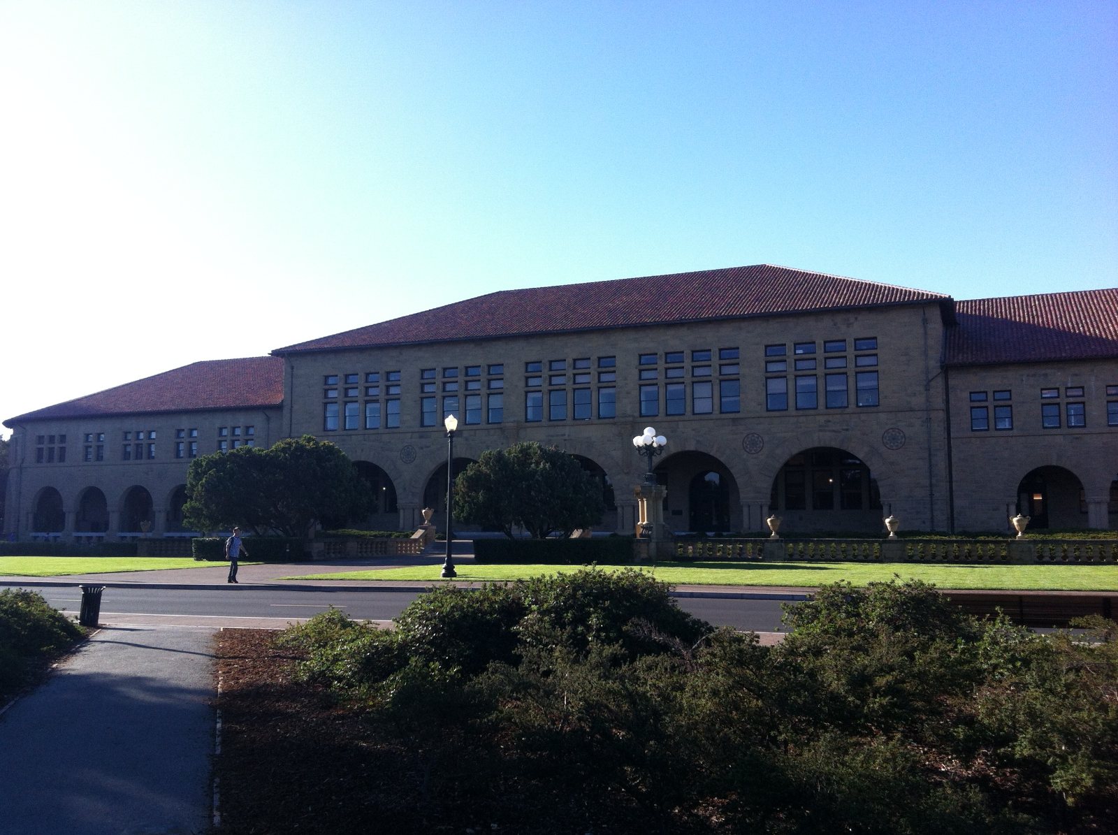 Zandstenen gebouw met rode pannendaken en bogen op de campus van Stanford University, onder een strakblauwe lucht.