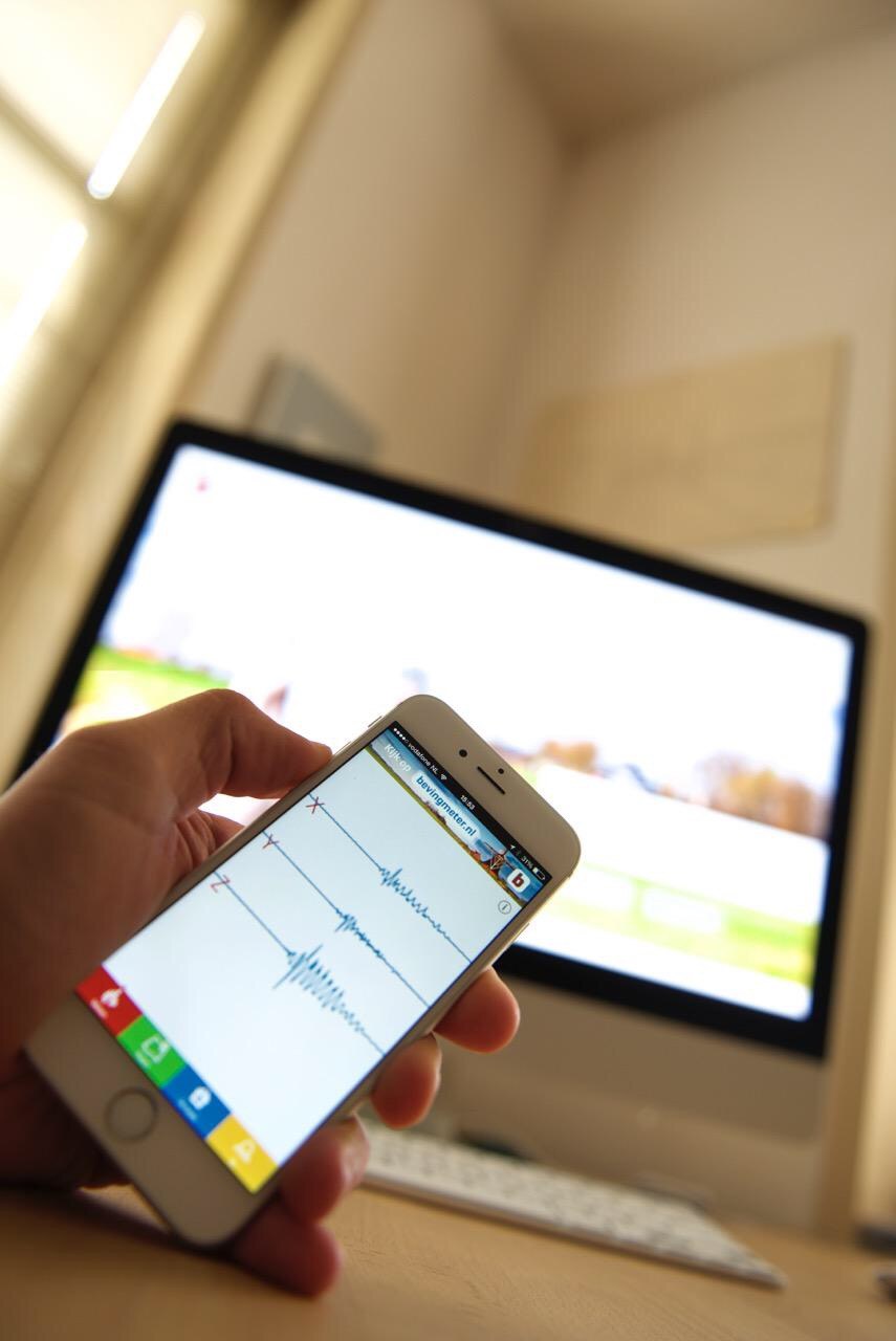 De Bevingmeter-app op een iPhone toont drie seismogrammen (x, y, z) met een uitslag; op de achtergrond de website bevingmeter.nl.