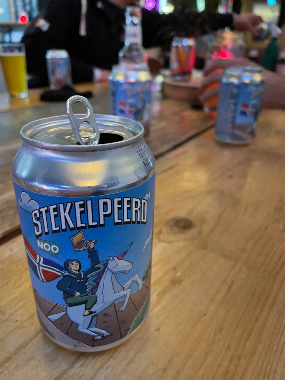 Blikje Stekelpeerd-bier van de NOO op een houten tafel: een eenhoorn met een ruiter die een laptop en de Groninger vlag draagt.